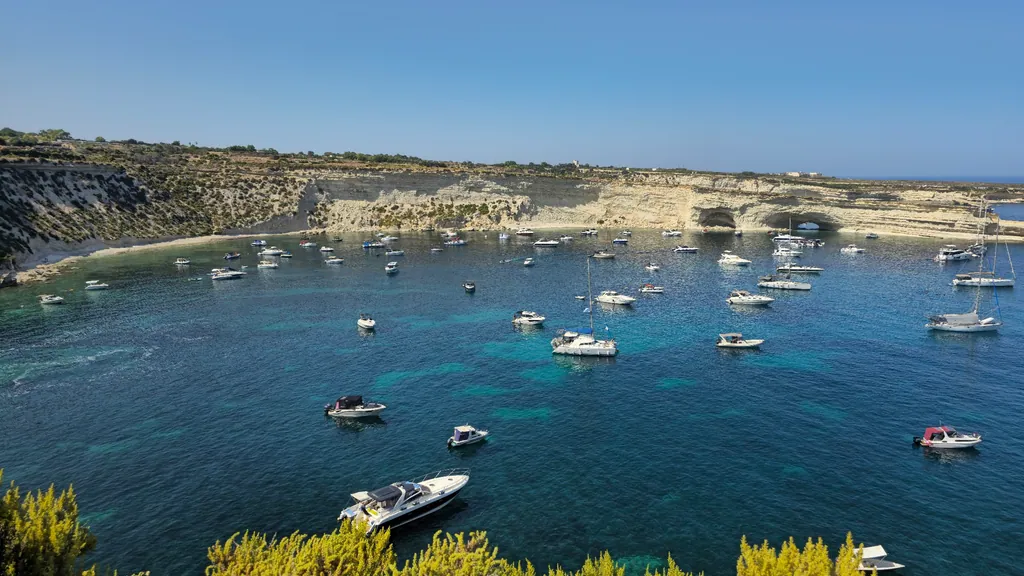 Boats anchored in a clear bay below the cliffs of north-west Malta